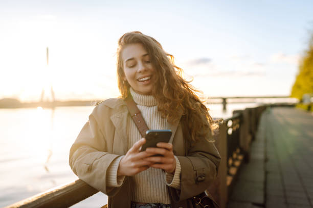 istock Young woman enjoys a sunny day by the river, using her smartphone. 2174156164