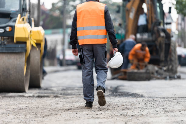 istock Construction worker in orange vest walks towards roadwork site during daytime in an urban environment with heavy machinery 2174156909