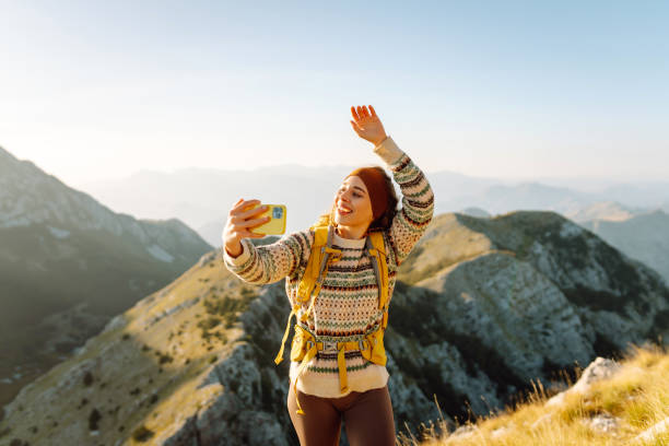 istock Young woman enjoying a hiking adventure while taking a selfie on a mountain summit during a sunny day. 2174157534