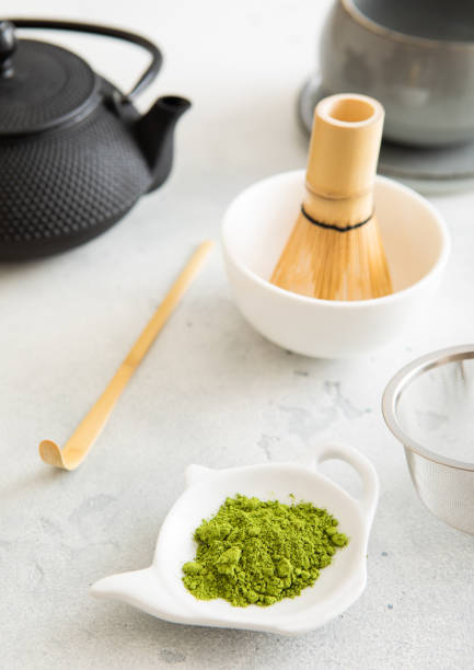 istock Matcha green tea powder with bamboo spoon and whisk in ceramic bowl with iron kettle on white background. 2174163741