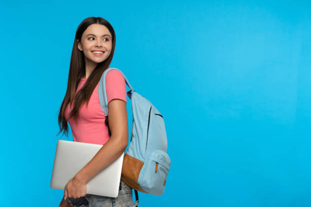 Attractive smiling girl high school female pupil student teenager in casual clothing with backpack holding using laptop, going to school with computer copy space isolated on blue background atractiva chica sonriente de la escuela secundaria, alumna estudiante, adolescente en ropa informal con mochila que sostiene el uso de una computadora portátil, va a la escuela con el espacio de copia de la computadora aislado sobre fondo azul
