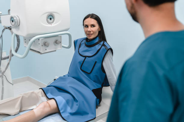istock Female patient in a protective suit lying on bed in modern X-ray machine for scanning her leg or knee for injuries and fractures looking at male doctor . The concept of medical technologies. 2174166937