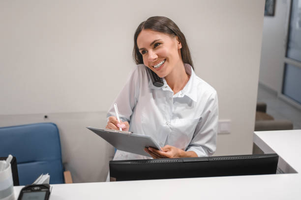 istock Female receptionist talking to patient on mobile phone, smiling, using computer at workplace, telling healthcare checkup test results, bringing good news, using modern technology for communication 2174168093