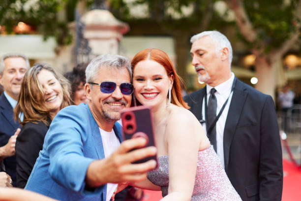 The actress approaches an eager fan and takes a selfie with him on the red carpet. A man and woman take a selfie with other people around them at the red carpet event. celebrity fans stock pictures, royalty-free photos & images