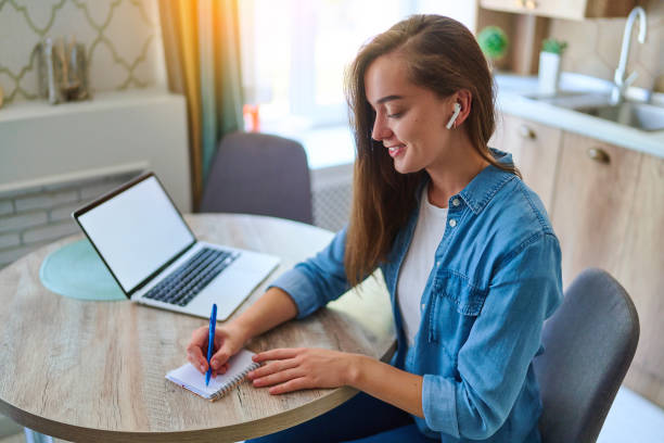 istock Happy young smart millennial woman takes a note with pen in a notepad and using laptop with open white blank display for online education at workspace. Computer mockup for website advertising 2174174616