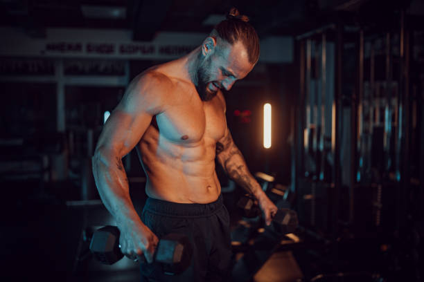 istock Muscular man lifting dumbbells in dimly lit gym. 2174180427