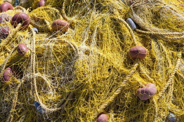 Yellow fishing nets in a pile on the coast in the port. Orange round buoys. Sunny summer day. Astrakeri, Corfu, Greece.