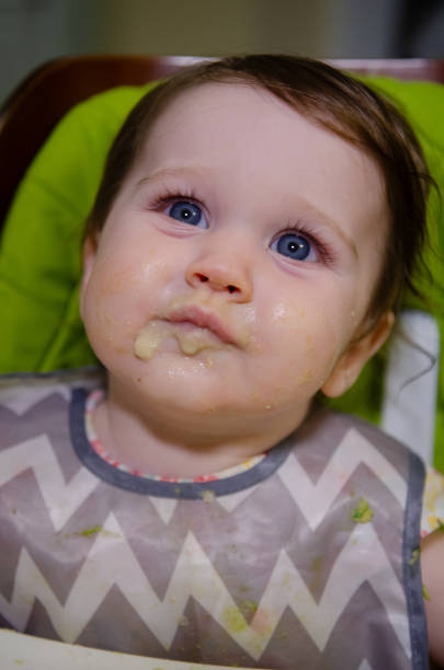 A seven month old girl sits in her chair eating.