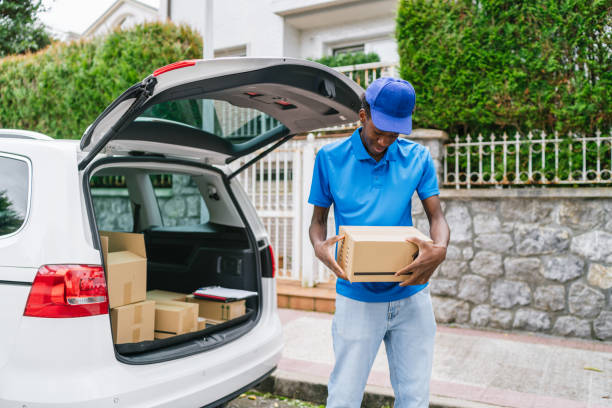 istock Young delivery man holding a cardboard box while standing by an open car trunk. 2174187494