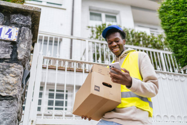istock Young African courier checking his phone while holding a package in a residential area 2174189171