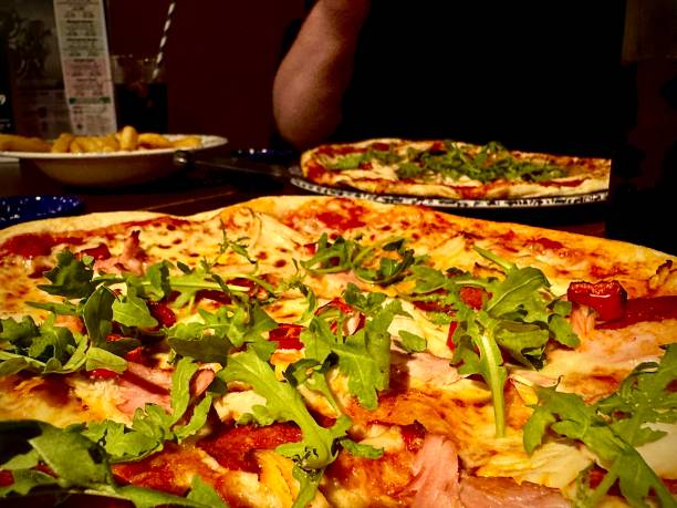 Freshly made pizza with ham, chicken, rocket leaves and peppers