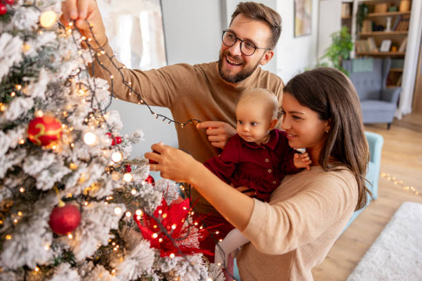 Young family decorating Christmas tree, placing Christmas lights on it