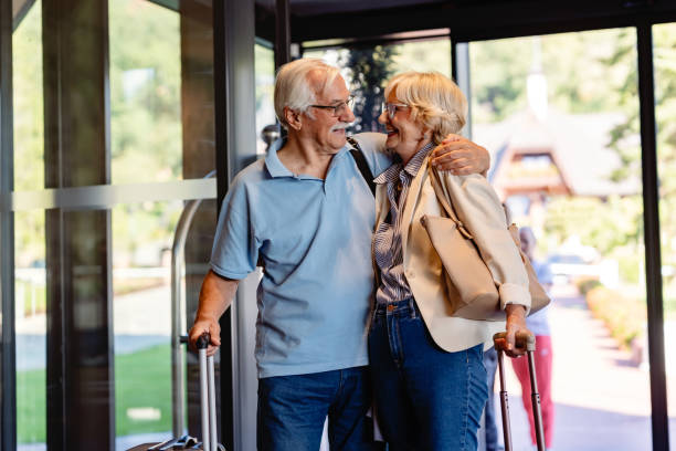 istock An elderly couple enters a hotel lobby, pulling their suitcases. They are dressed casually, smiling, and ready for travel, suggesting they are on a vacation or trip. 2174198906