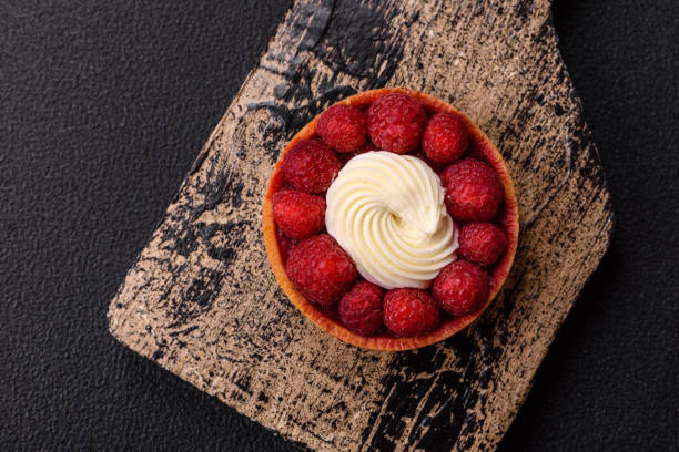 Sweet tartlet with raspberries and cream on a dark textured background