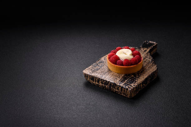Sweet tartlet with raspberries and cream on a dark textured background