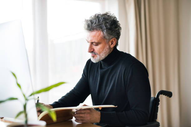 istock Handsome man in wheelchair working from home office, using computer in office. Telecommuting and home office. 2174215354