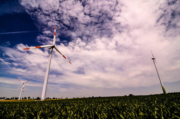 Two wind turbines are in a field with a cloudy sky in the background. Scene is peaceful and serene, as the turbines are surrounded by a lush green field