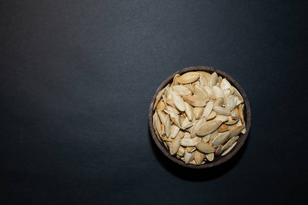 Roasted, salted pumpkin seeds in a bowl on a black background.