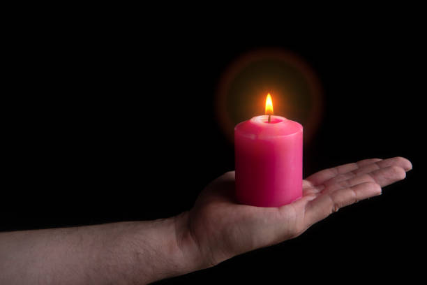 istock Outstretched man's hand holding a lit red candle against black background 2174254543