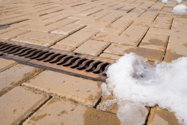 Fragment of sidewalk with drainage grate and remnants of snow. Yellow pavement tiles, protective decorative metal grate for draining melted, rainwater. Urban infrastructure, winter maintenance