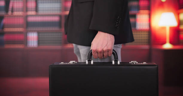 istock Midsection Of Lawyer Carrying Briefcase Against Bookshelf 2174258974