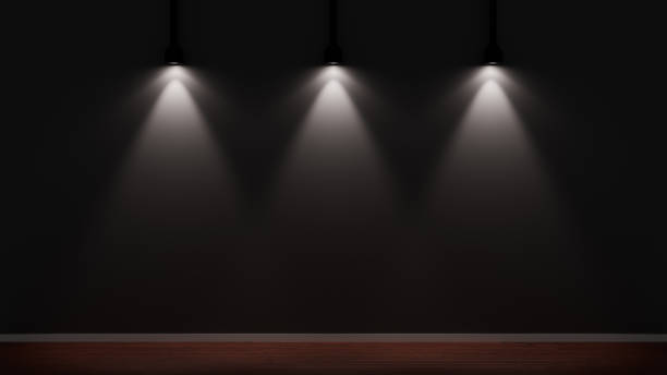 Three spotlights dramatically illuminate a black wall in a dark studio with a wooden floor