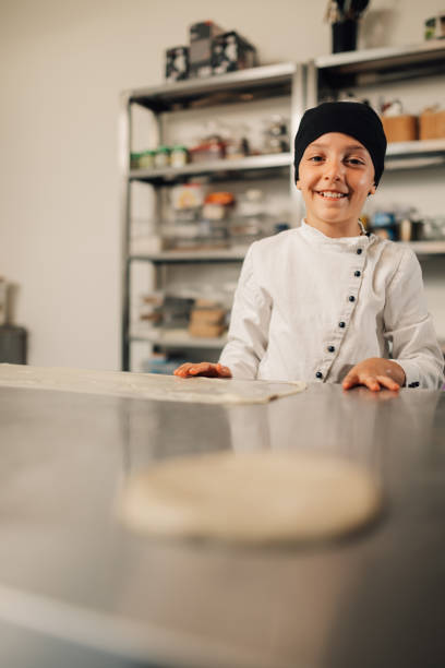 istock Smiling child girl chef stretching dough in steel kitchen work environment 2174278955