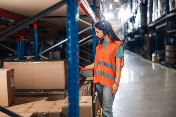 istock Female warehouse worker with headset scans boxes in large storage area 2174278997