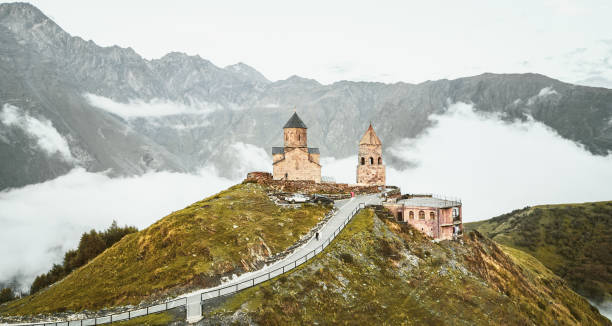 istock Aerial view Gergeti trinity church after sunset, Georgia. Stepanstminda famous sightseeing landmark on hilltop with misty caucasus mountains background. Tourist visit popular sightseeing attraction 2174292402