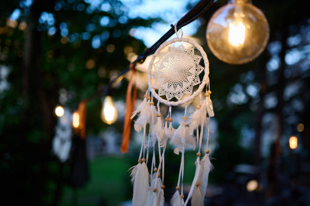 istock Dreamcatcher with soft feathers hanging under glowing lights in the evening, creating a warm and mystical atmosphere. Ideal for boho, spiritual, or cozy outdoor design themes 2174294188