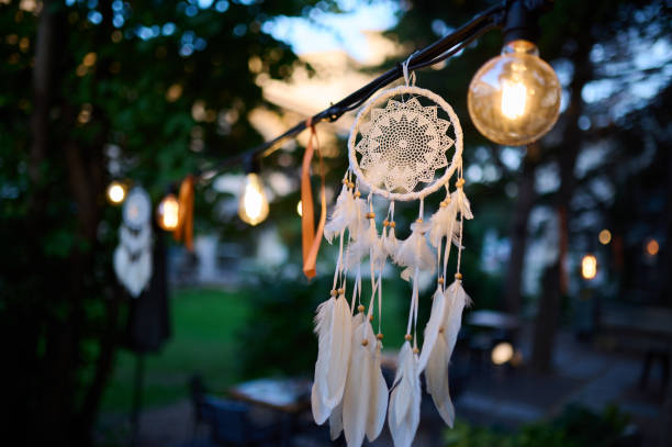 Dreamcatcher with soft feathers hanging under glowing lights in the evening, creating a warm and mystical atmosphere. Ideal for boho, spiritual, or cozy outdoor design themes