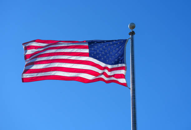 istock waving USA flag on pole against blue sky 2174296502