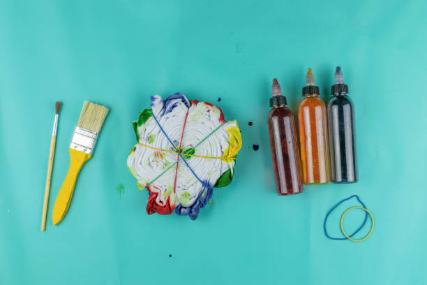 istock Tie-Dye Crafting Materials: Paintbrushes, Tie-Dyed Fabric, Dye Bottles on Blue Surface 2174302941