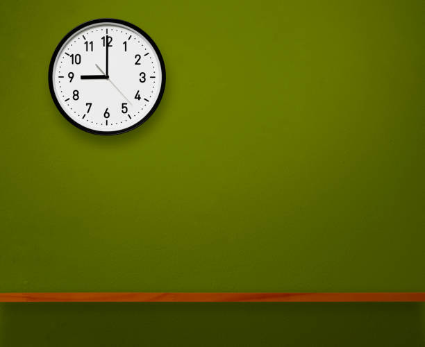 9 O'Clock wall clock above the wooden shelf on green concrete wall with copy space.