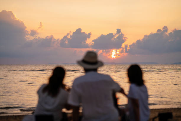 Three mid adult friends watching the sunset on a beach