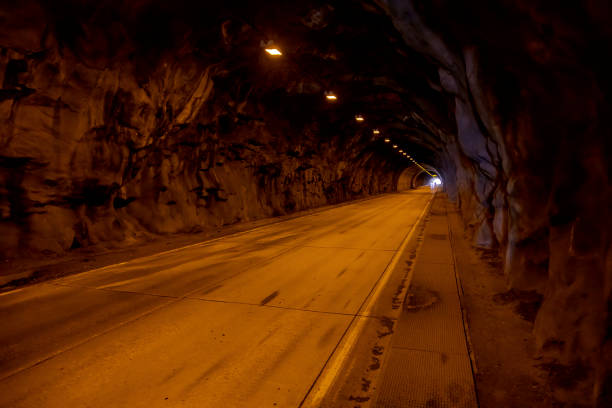 Illuminated tunnel on Big Oak Flat Road in Yosemite National Park, California. The long, straight passage through solid rock features warm lighting and a smooth road surface, creating an atmospheric scene.