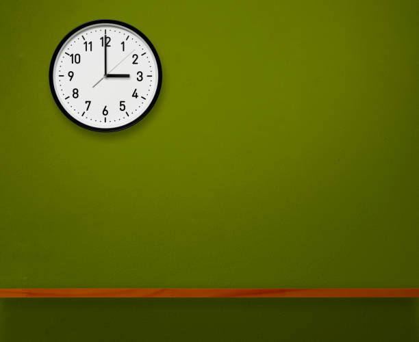 3 O'Clock wall clock above the wooden shelf on green concrete wall with copy space.