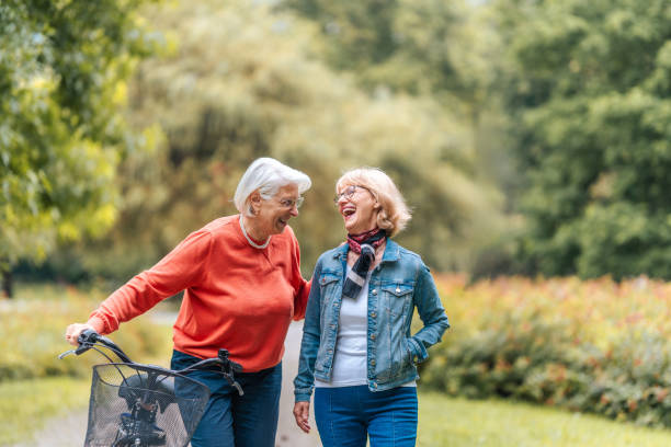 Senior Women Sharing Laughs During Park Stroll with Bicycle