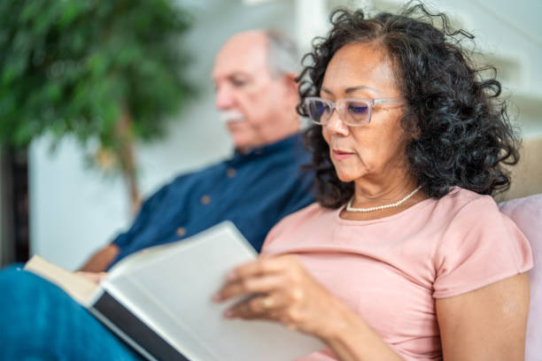 istock Interracial Elderly Couple Relaxes with Book and Laptop 2174331484