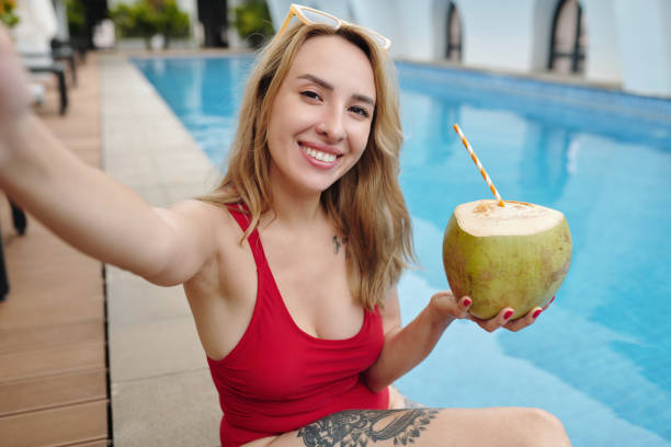 istock Smiling Woman Taking Selfie by Pool Holding Coconut Drink 2174336979