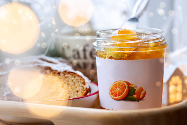 Homemade orange jam in a jar, a plate with a cupcake and a cup of coffee. Festive blurred lights of the garland. Selective focus.