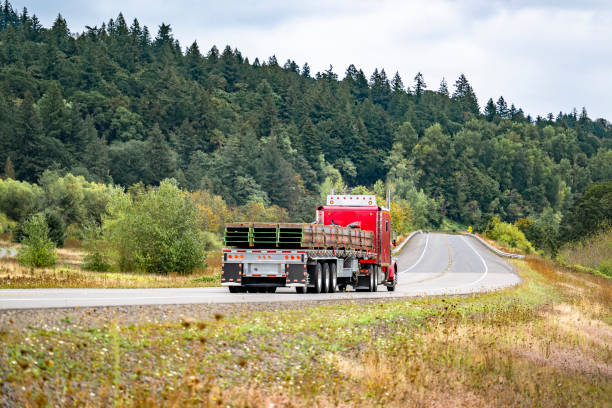 istock Classic big rig red semi truck with extended cab transporting fastened metal cargo on flat bed semi trailer driving on the narrow winding road 2174344583