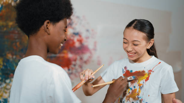 istock Smiling diverse children paint color on each other shirt at wall. Edification. 2174352988