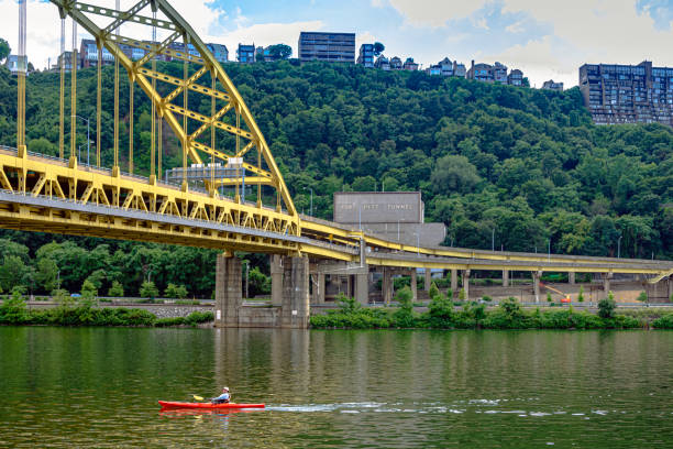 Pittsburgh, Pennsylvania, USA-July 30, 2016: Fort Pitt Bridge over the Monongahela River with Mt. Washington and the Fort Pitt Tunnel in the background and a kayaker in the foreground.