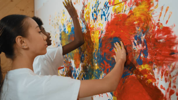 istock Girl and african boy paint the wall with their hand. Side view. Edification. 2174363824