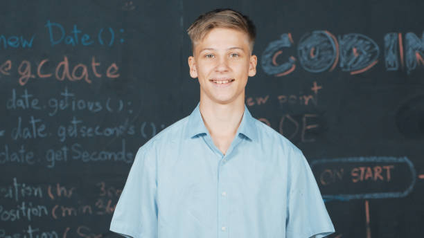 istock Smiling teenager looking at camera while standing at blackboard. Edification. 2174365245