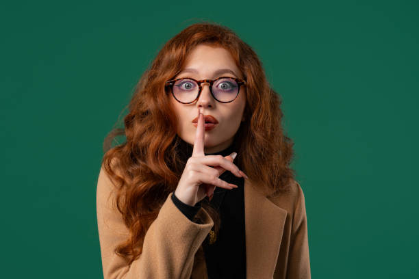 istock Attrcative ginger woman with finger on lips - shh, secret, silence, green studio 2174367188
