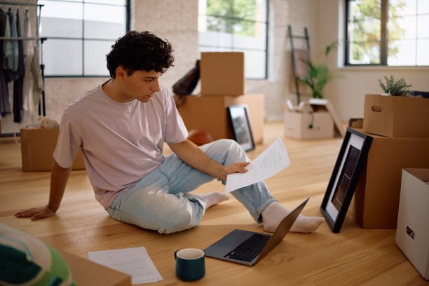 istock Young man doing taxes and using laptop while moving into new house. 2174377464