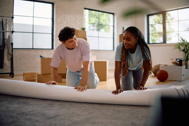 istock Happy multiracial couple unrolling carpet while moving into new home. 2174378433