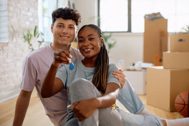 istock Happy multiracial couple holding house key while moving in together and looking at camera. 2174378614
